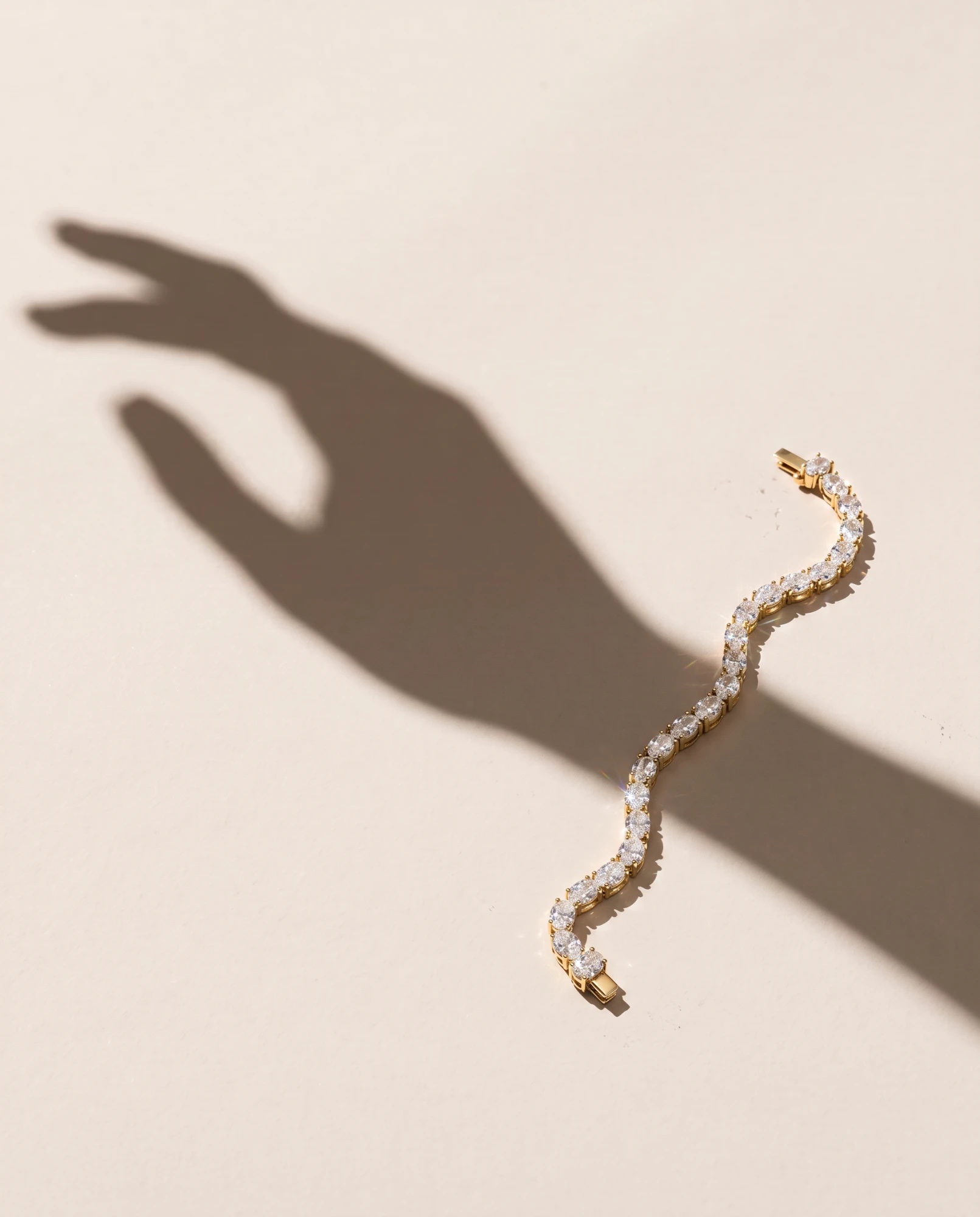 A gold diamond tennis bracelet beside the shadow of a hand